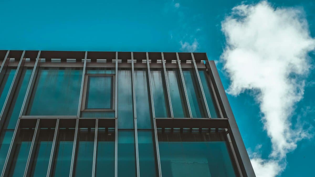 Low angle view of a modern office building with glass facade against blue sky with clouds.