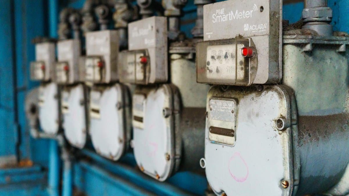 Multiple smart utility meters lined up on a blue industrial wall.