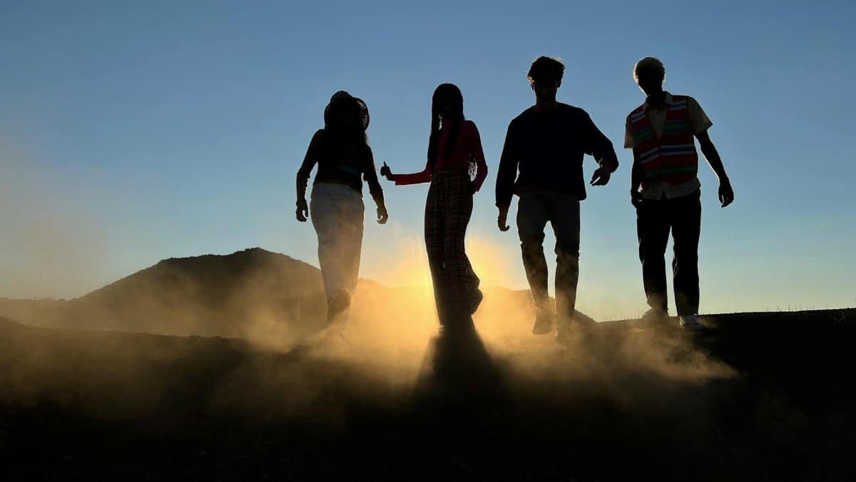 Four people silhouetted against a setting sun, walking outdoors in a dusty landscape.