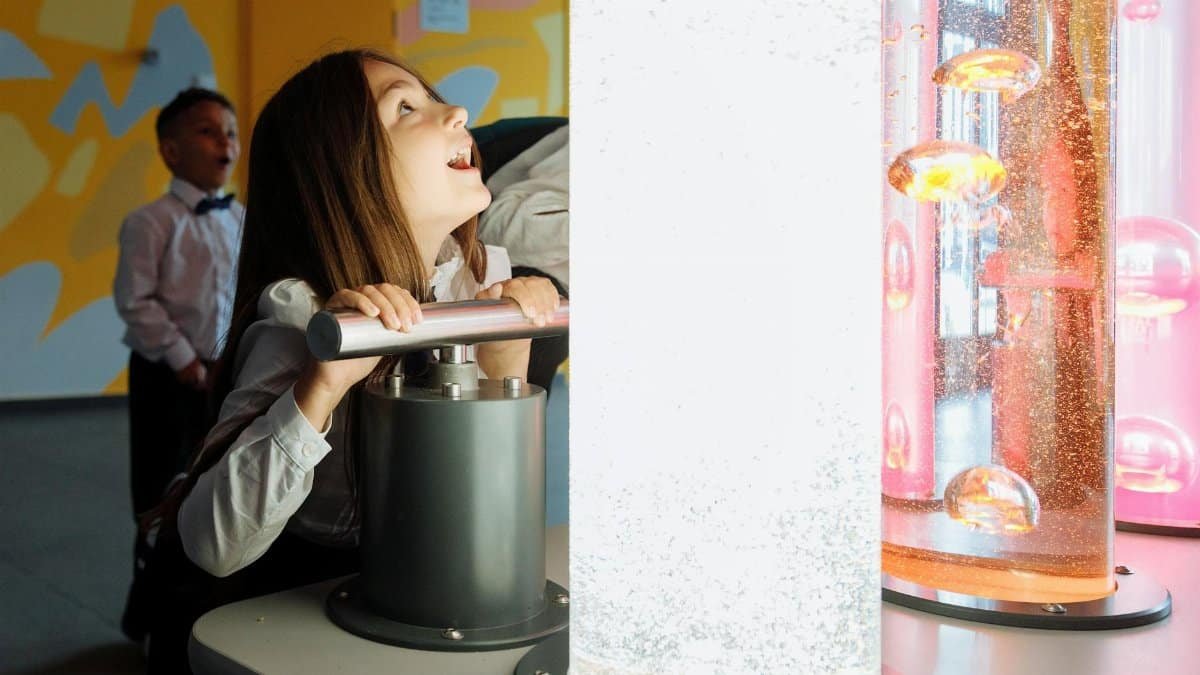 Children engage with interactive science exhibit featuring colorful liquids and lights.