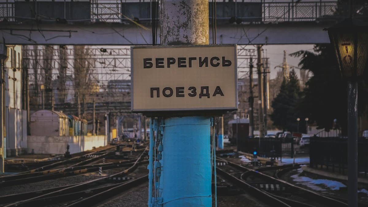 Close-up of a railway warning sign with Russian text against an urban infrastructure backdrop.