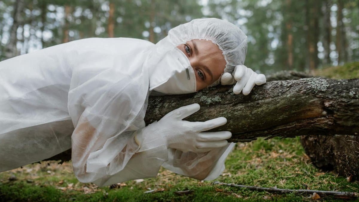 Scientist in protective suit lying on a tree trunk in the forest, emphasizing ecology and nature protection.