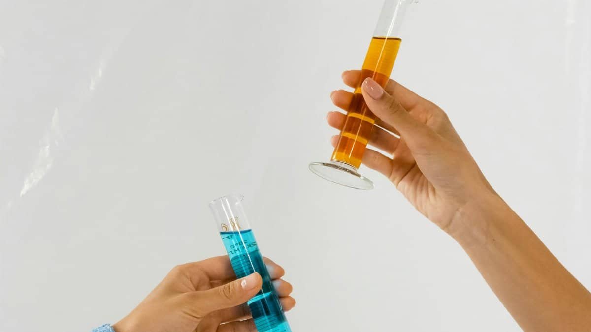 Close-up of hands holding graduated cylinders with blue and orange liquids, symbolizing scientific research.