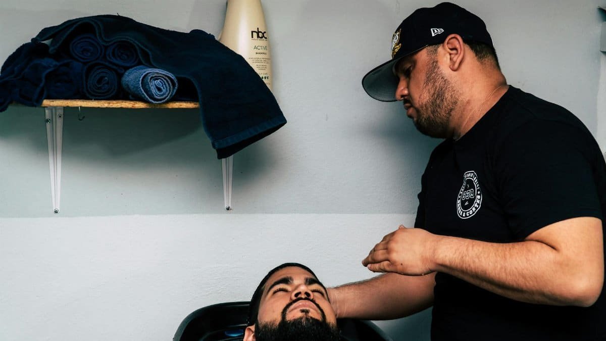 A barber grooming a client's beard in a modern barbershop setting.