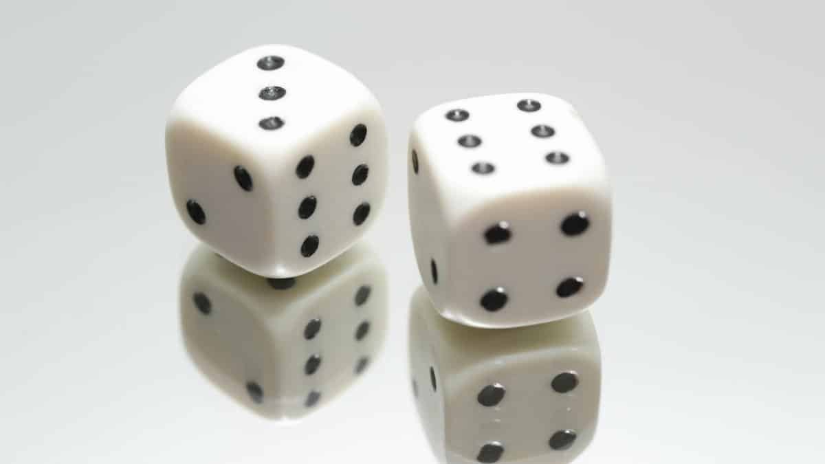 A close-up view of two white dice with reflection on a smooth white surface, symbolizing luck and chance.