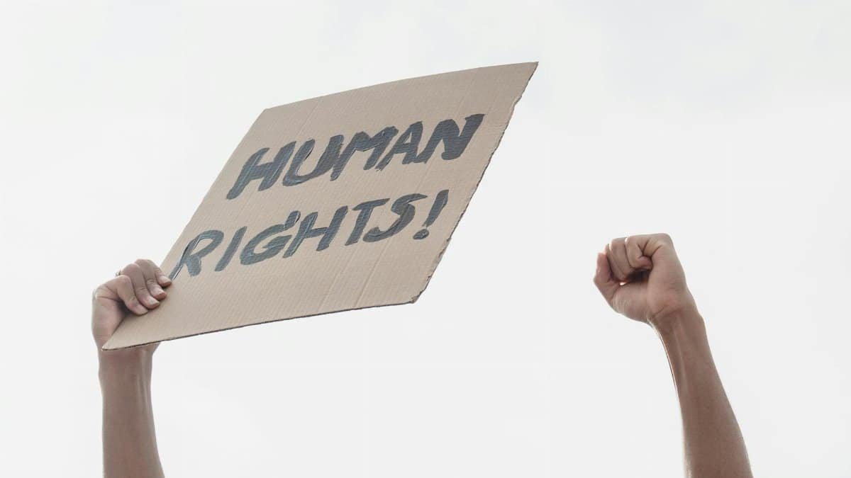 Raised clenched fists holding a sign advocating for human rights in a protest setting.