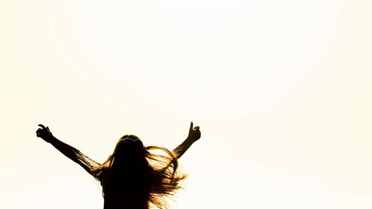 Backlit silhouette of a woman with arms up, capturing freedom and joy in a minimalist setting.