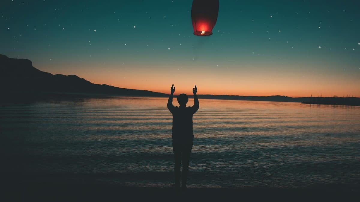 Silhouette releasing a floating lantern by a peaceful lake at sunset, creating a serene and magical atmosphere.