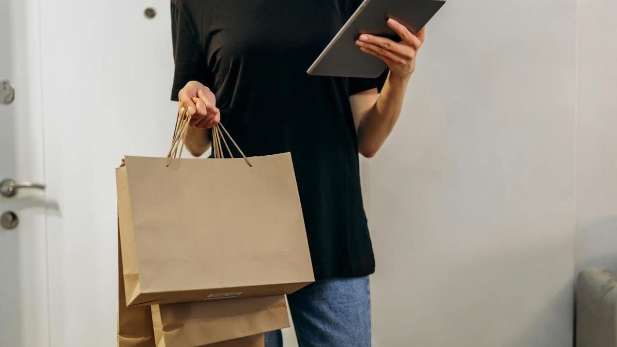 Woman in black shirt with shopping bags using a tablet at home, symbolizing online shopping convenience.