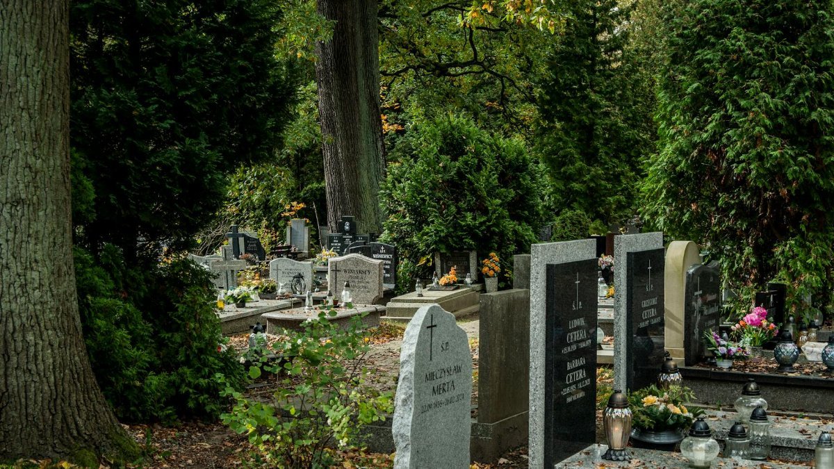 Peaceful cemetery with headstones surrounded by green trees and flowers.