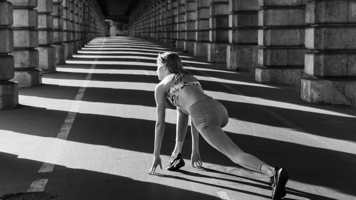 Woman stretching under urban bridge in monochrome capturing dynamic sport pose.
