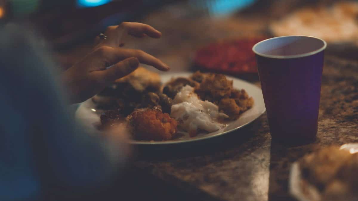 Close-up of a hand reaching for delicious food on a Thanksgiving dinner plate indoors.