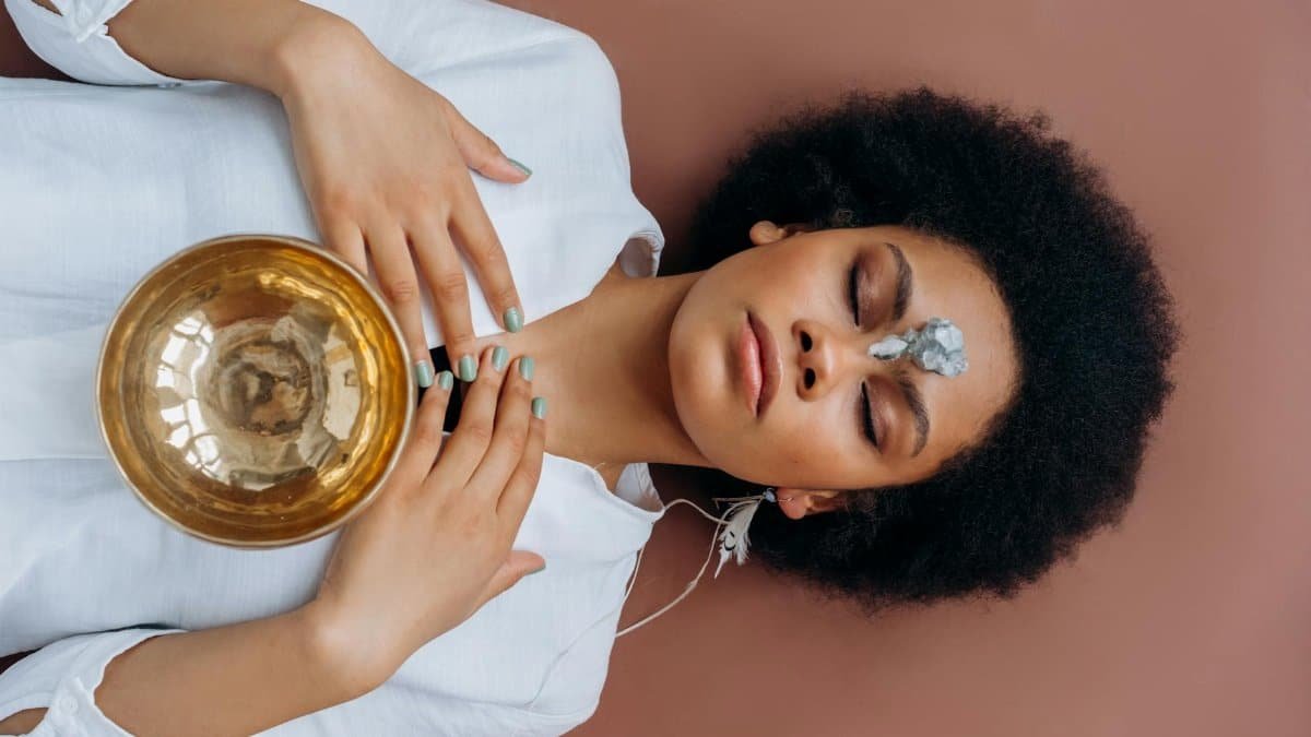 A woman meditates with a Tibetan singing bowl and crystals, promoting wellness and spiritual healing.