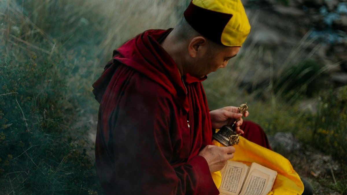 Monk engaging in spiritual practice outdoors, holding ritual bell and scripture, capturing serenity and devotion.