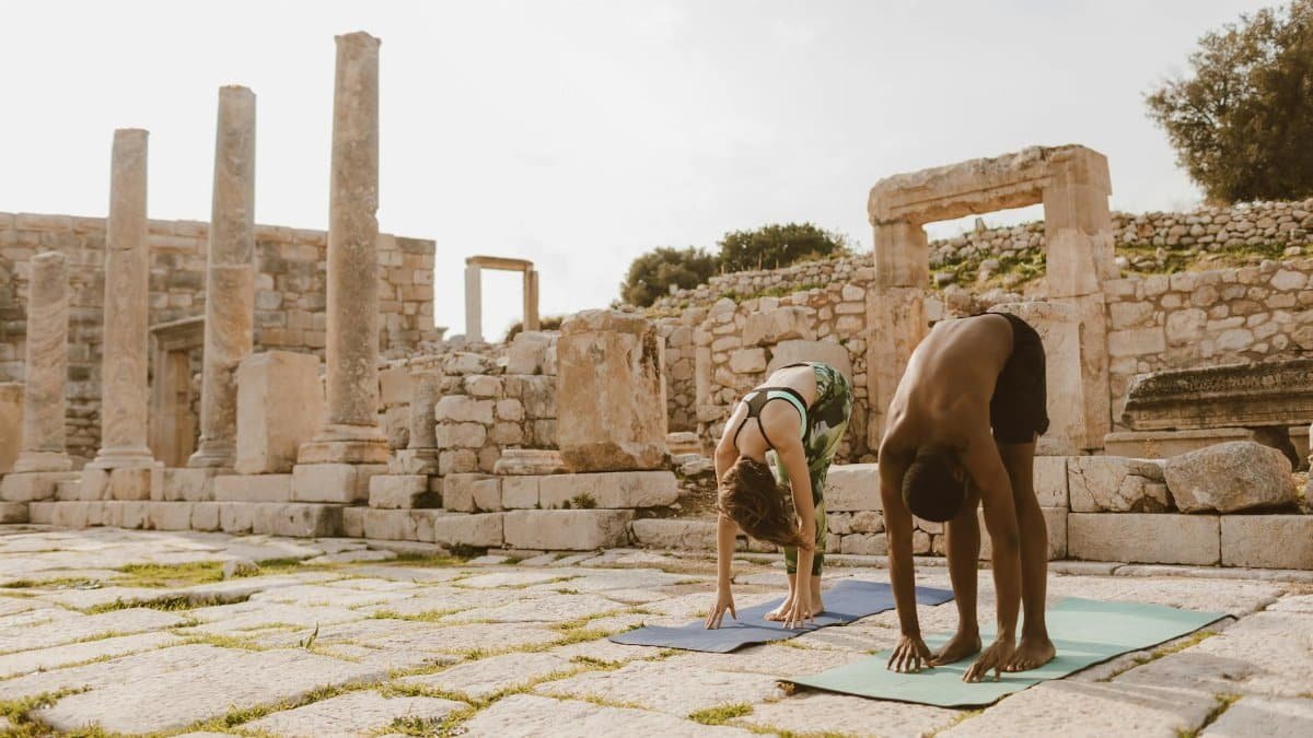 Two people practicing yoga outdoors among ancient ruins, emphasizing relaxation and flexibility.