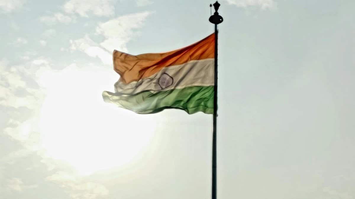 Indian national flag waving on flagpole against a bright sky with clouds.