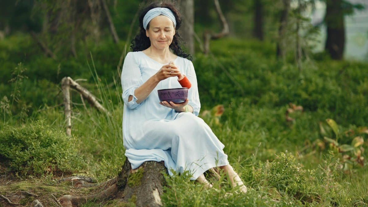 A woman practicing mindfulness with a singing bowl in a serene forest setting, embracing relaxation.