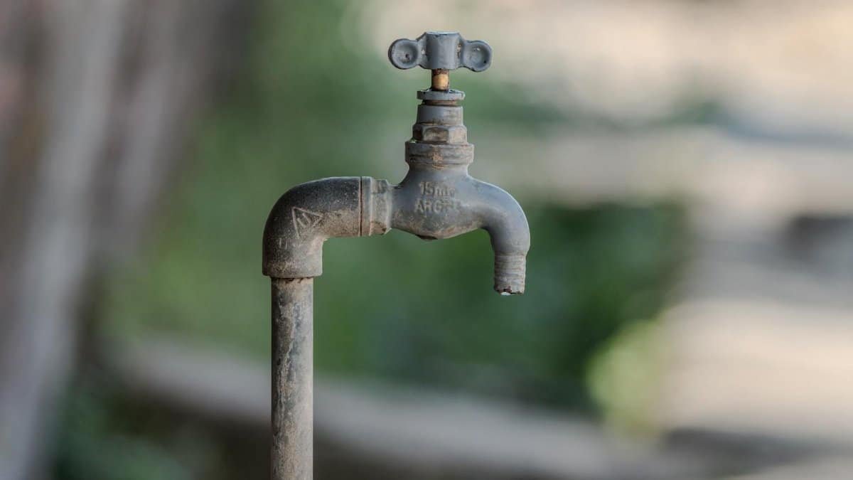 Close-up of a weathered outdoor water faucet with green blurred background, symbolizing water conservation.