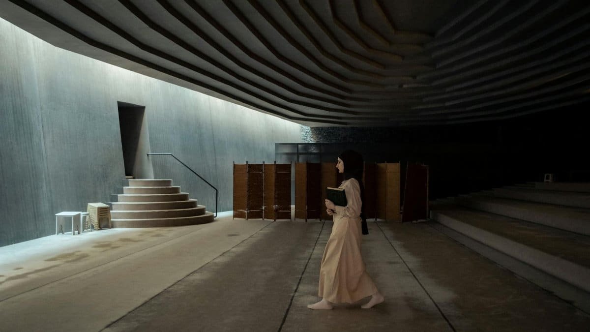 Muslim woman walking barefoot inside Sancaklar Mosque with a book.