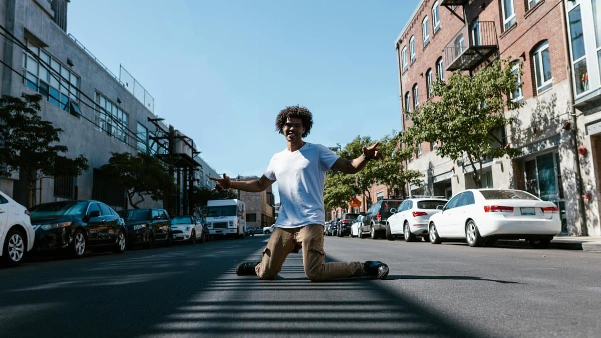 Dynamic portrait of a man dancing freely in an urban setting with parked cars lining the street.