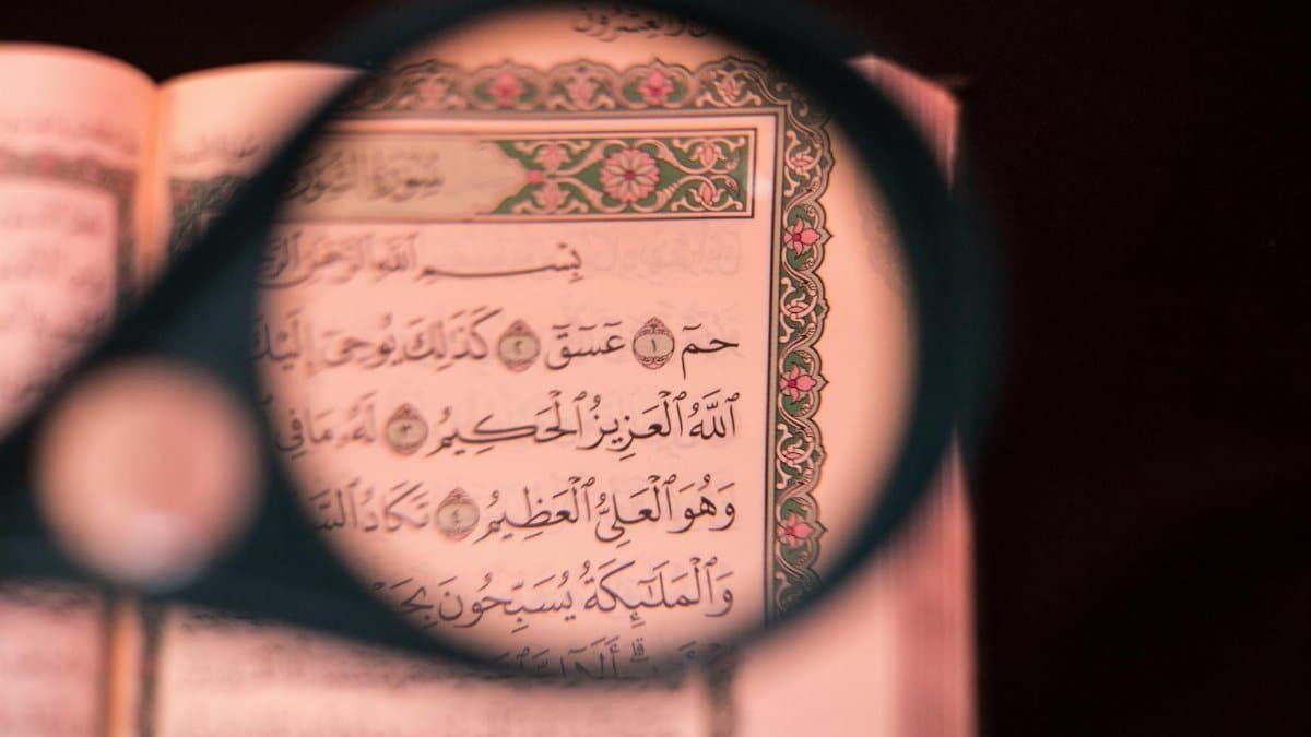 Close-up of Quranic verse through magnifying glass highlighting Arabic calligraphy.