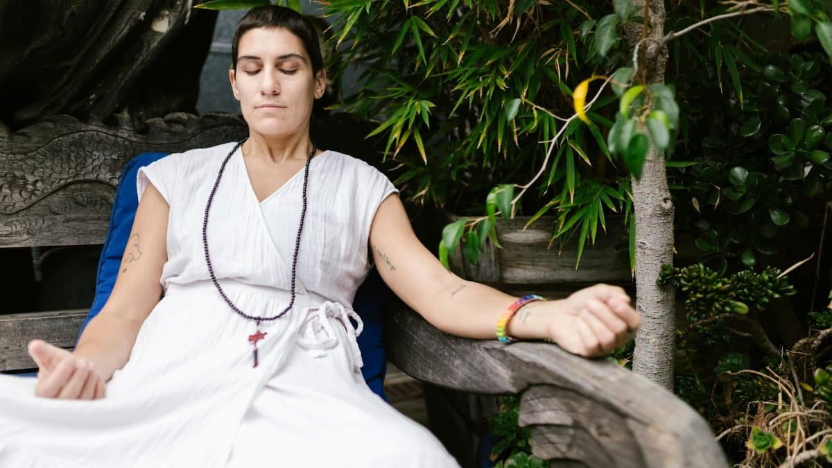 A woman in white dress meditates outdoors, embodying calmness and mindfulness.