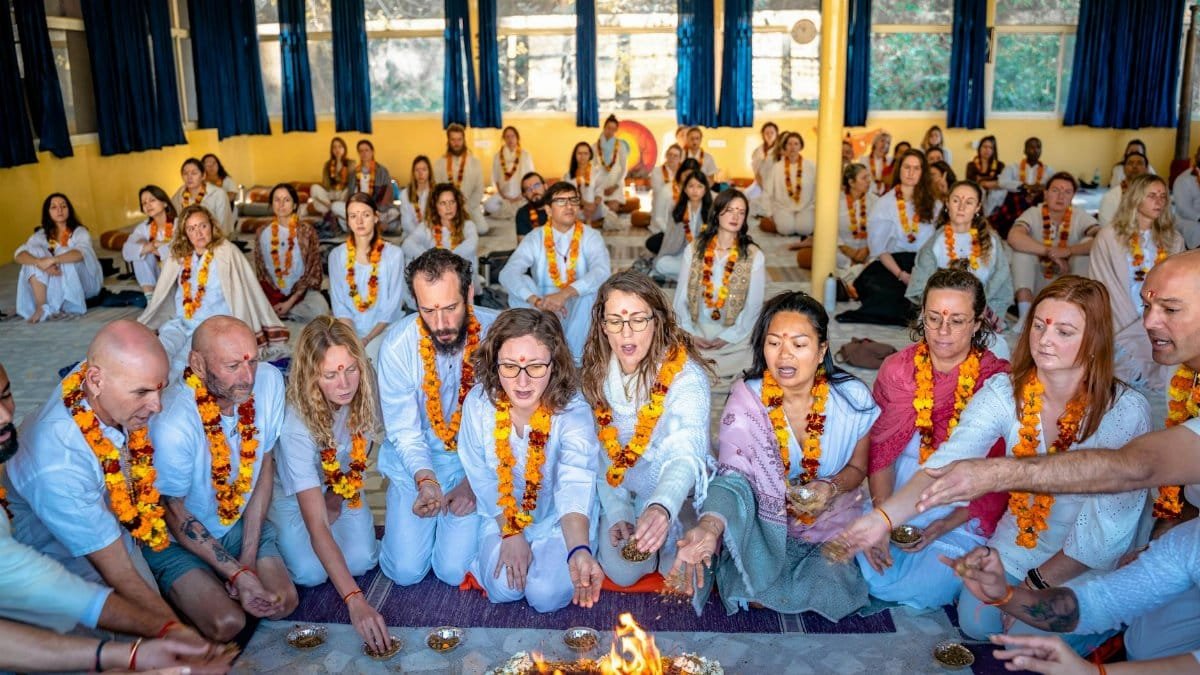 Group of people participating in a traditional fire ceremony in Rishikesh, India, wearing white clothes and garlands.