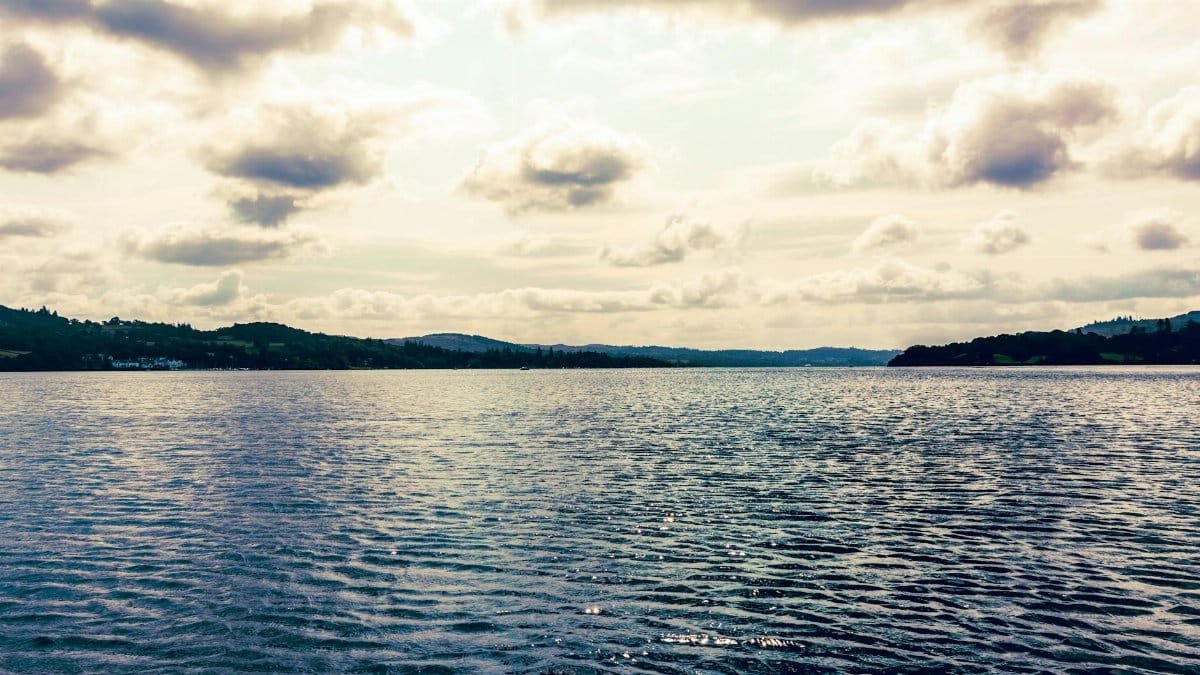 Peaceful Lake Windermere scene with calm waters and dramatic clouds in the scenic Lake District, England.