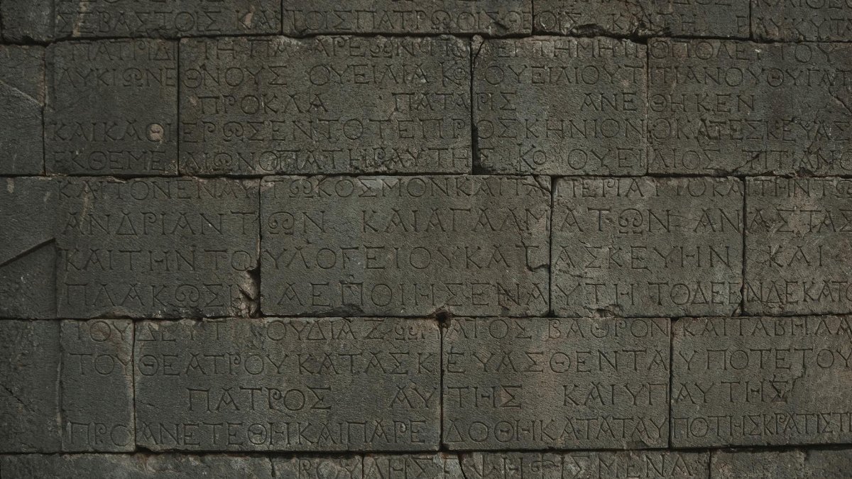Close-up of an ancient stone wall with Greek inscriptions engraved on it.