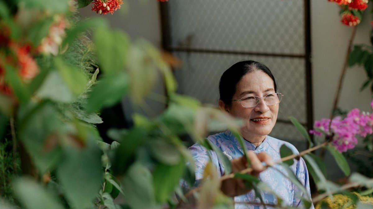 A senior woman enjoys colorful flowers in a vibrant garden setting.