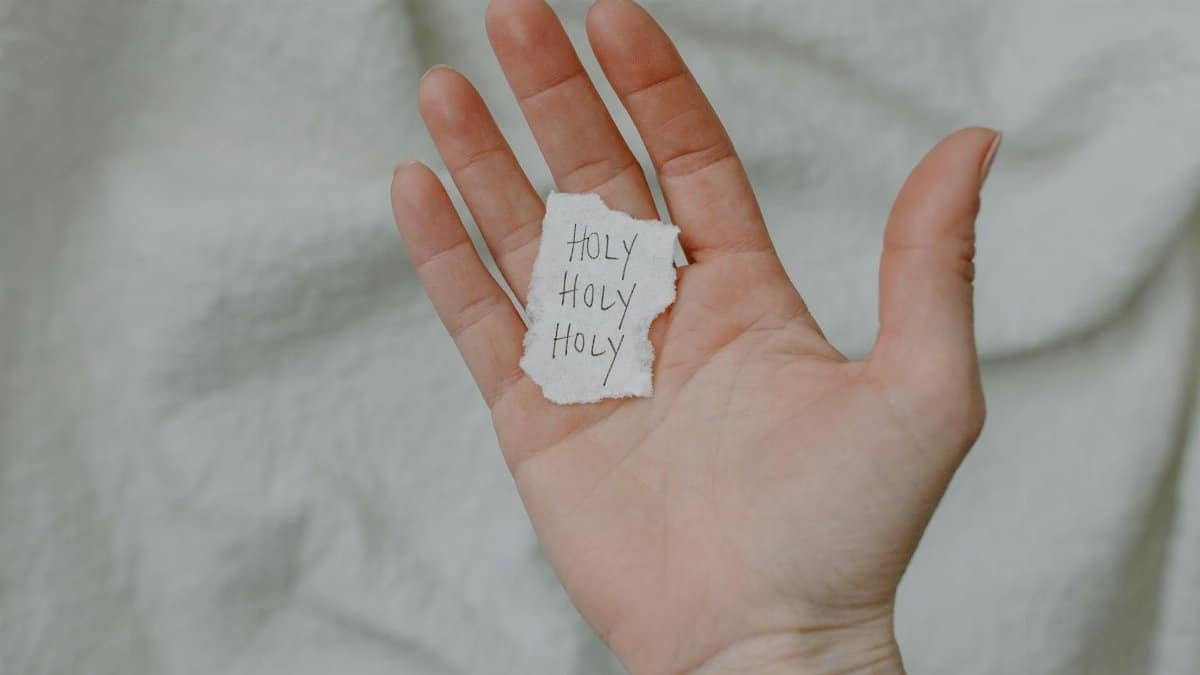 A close-up of a hand holding a paper with 'Holy' written, showing a spiritual theme.
