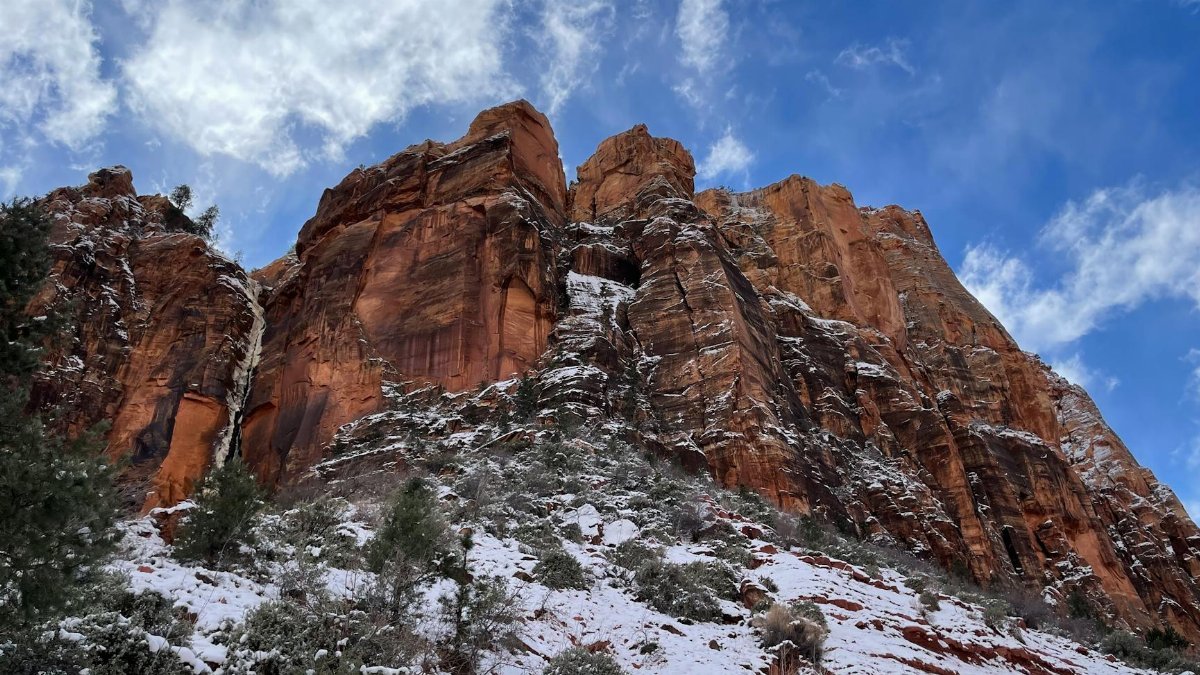 Majestic red cliffs at Zion National Park dusted with snow under a bright blue sky, showcasing nature's beauty.