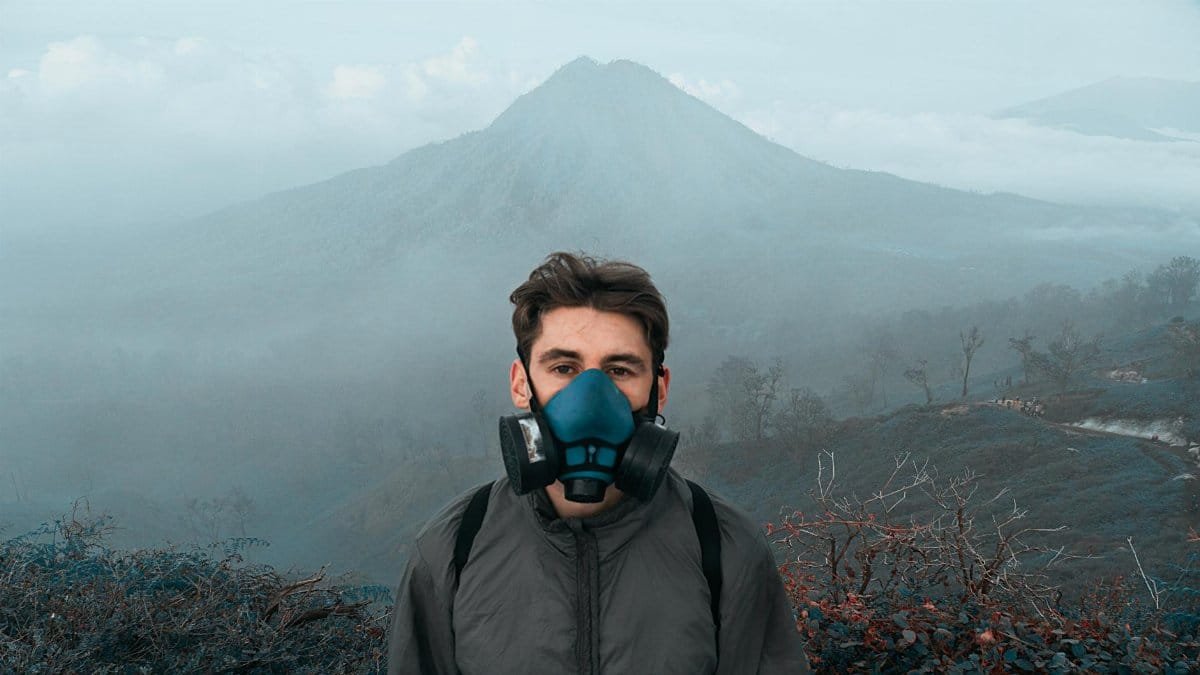 A man with a respirator mask stands in a misty mountain landscape, suggesting environmental awareness and adventure.