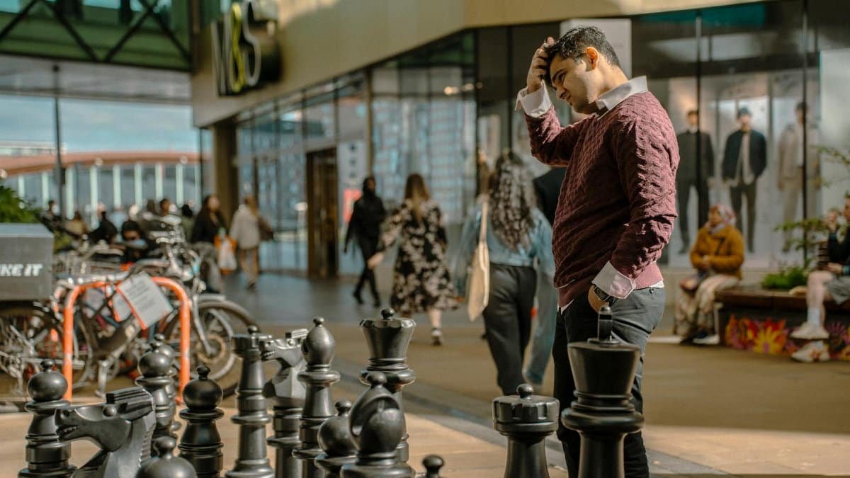 Man pondering over a large outdoor chess game in a bustling London area.