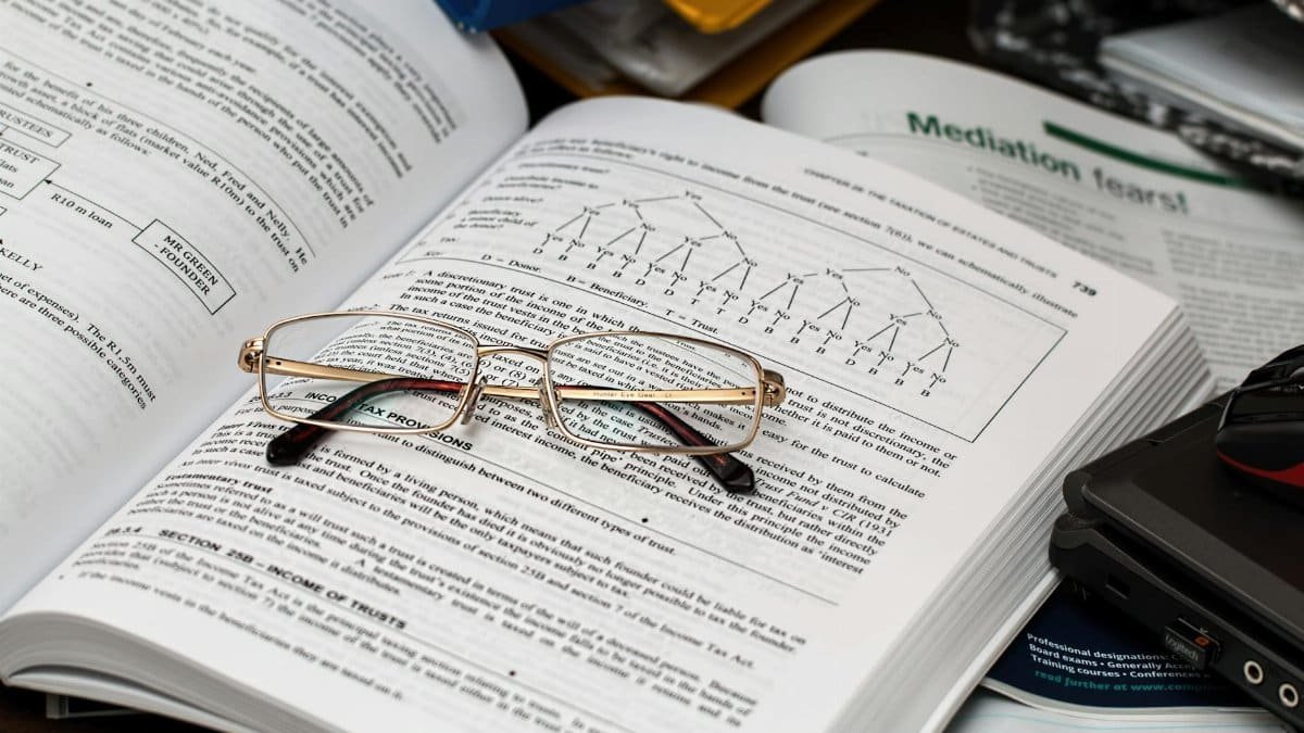 An open book with reading glasses, surrounded by study materials and a laptop, ideal for education themes.