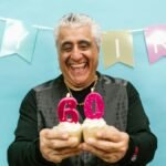 Smiling senior man holding cupcakes with 60 candles at a birthday party.