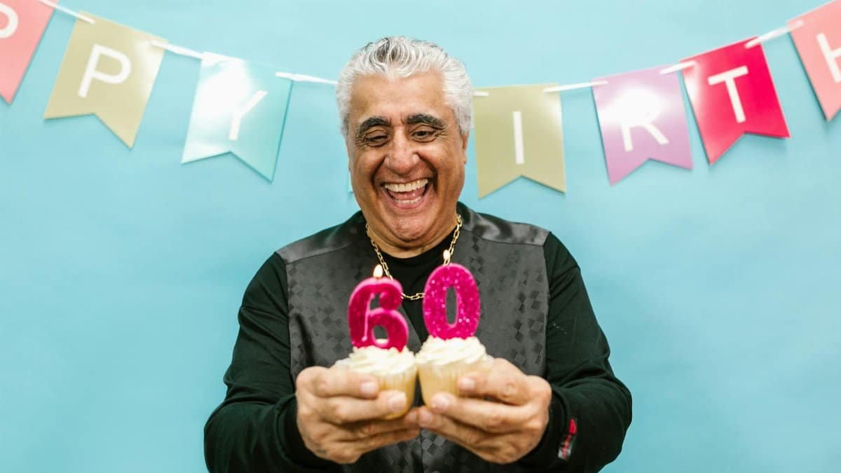 Smiling senior man holding cupcakes with 60 candles at a birthday party.