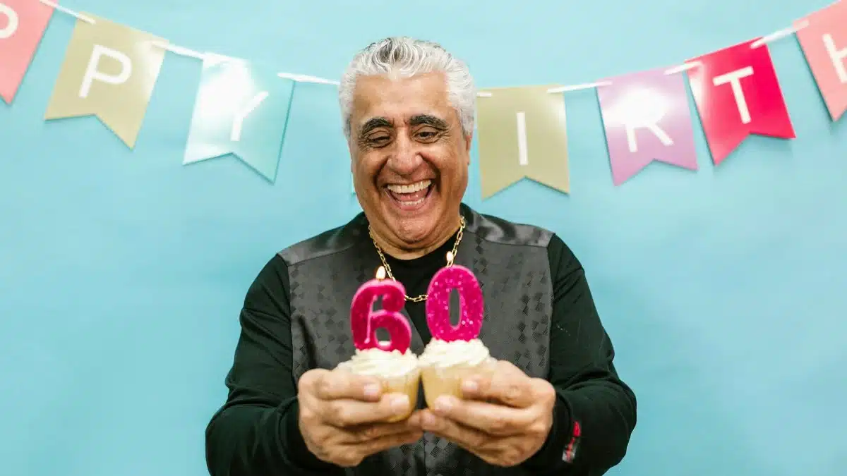 Smiling senior man holding cupcakes with 60 candles at a birthday party.
