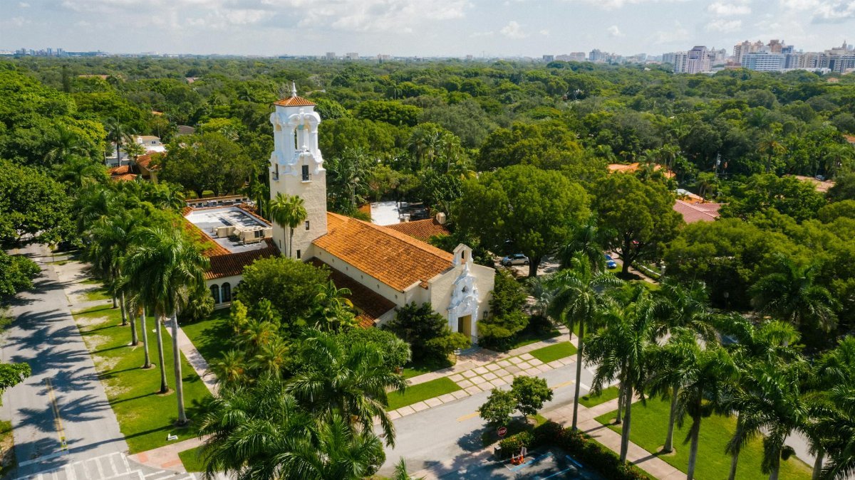 Aerial photo of a church in Coral Gables, Miami, surrounded by lush trees and urban landscape.