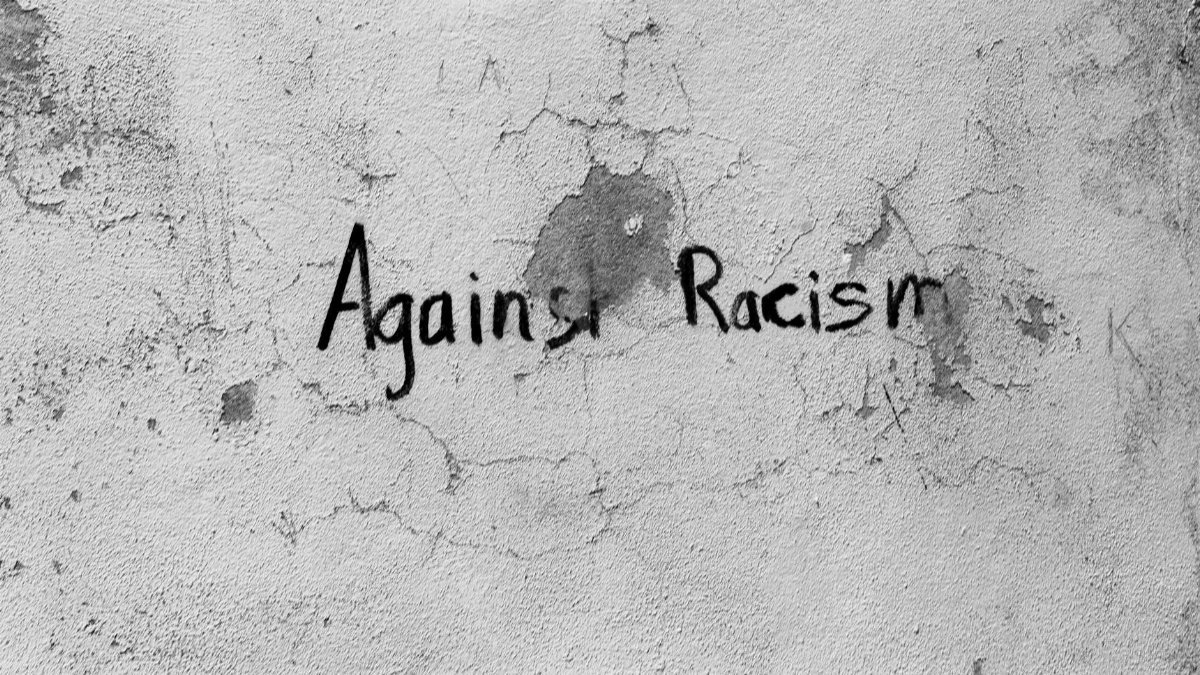 Black and white graffiti on a cracked wall with the message 'Against Racism' in Guarda District, Portugal.