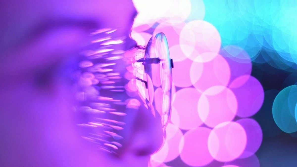 Close-up photo of eyeglasses with bright purple and blue bokeh lights creating an abstract aesthetic.