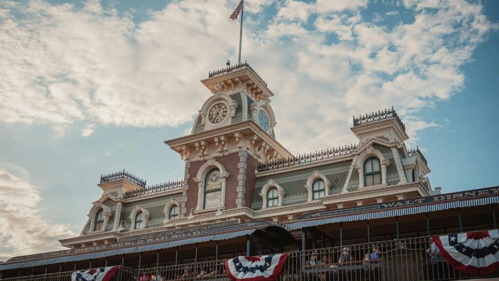 Iconic entrance to Walt Disney World Railroad at Magic Kingdom, Orlando, Florida, with vintage architecture and American flags.