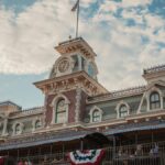 Iconic entrance to Walt Disney World Railroad at Magic Kingdom, Orlando, Florida, with vintage architecture and American flags.