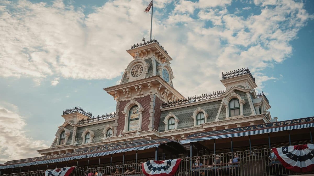 Iconic entrance to Walt Disney World Railroad at Magic Kingdom, Orlando, Florida, with vintage architecture and American flags.