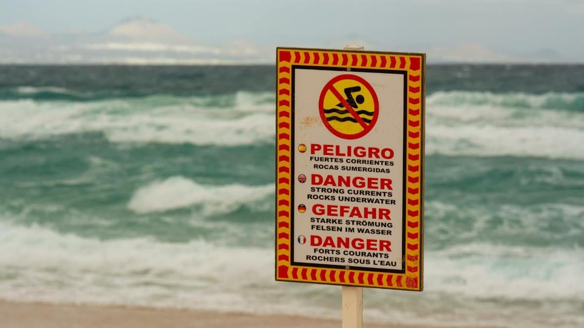 A beach warning sign cautioning about strong underwater currents in multiple languages.