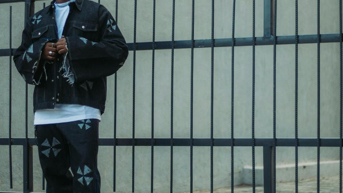 Fashionable young man wearing denim stands confidently against modern gate.