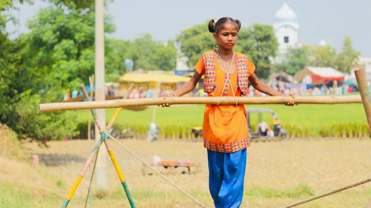 A young girl skillfully performs a balancing act on a tightrope in an outdoor setting, showcasing her talent.