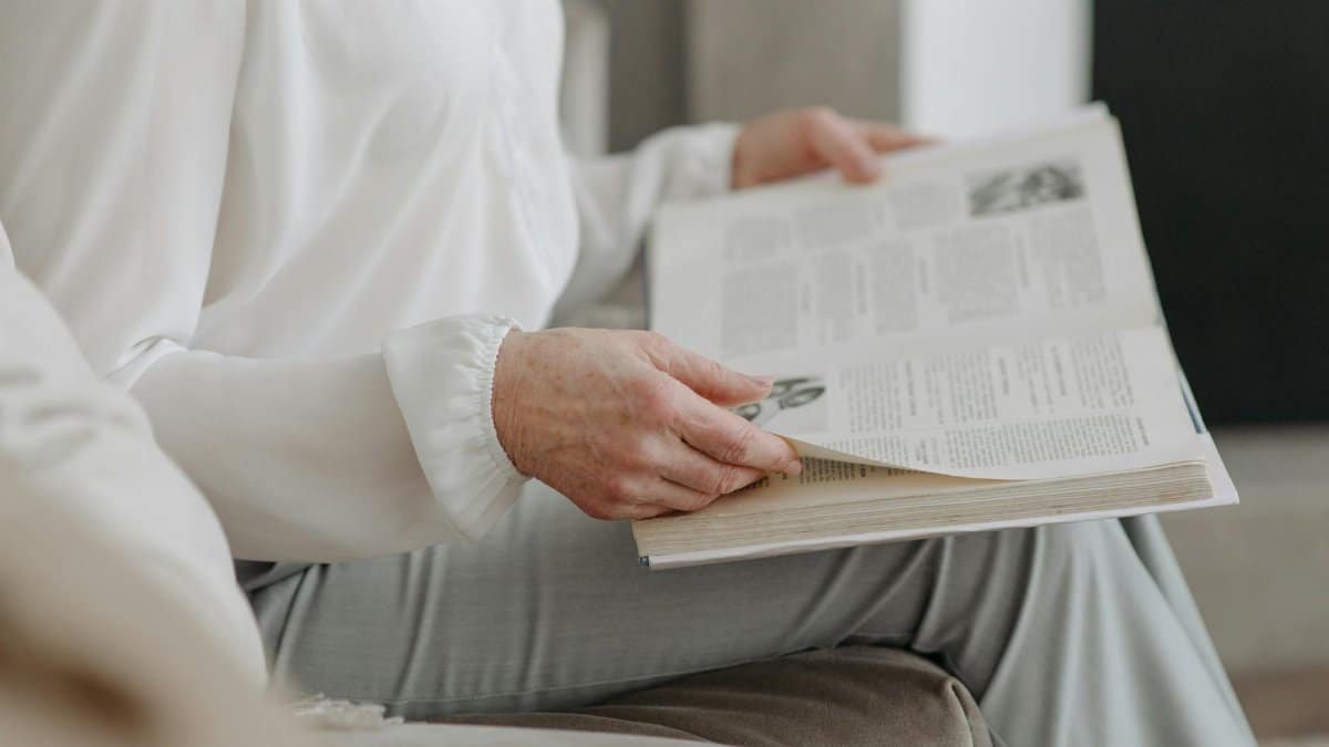 A senior adult in white attire reading a book while sitting indoors.