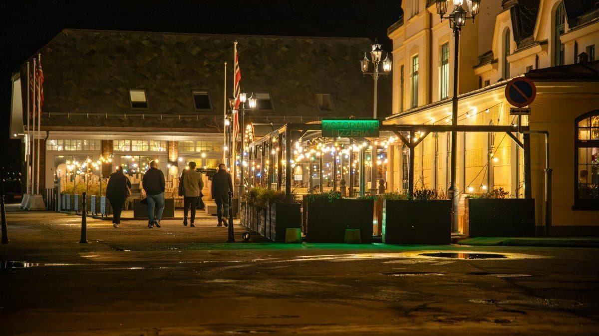 Vibrant night view of Ålesund's downtown with illuminated street restaurant and five people walking.