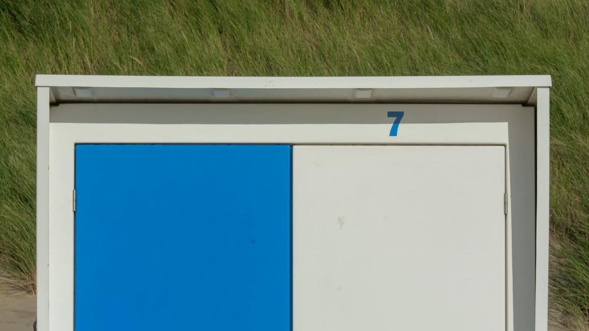 Close-up of a blue and white beach shed numbered seven against a grassy backdrop.